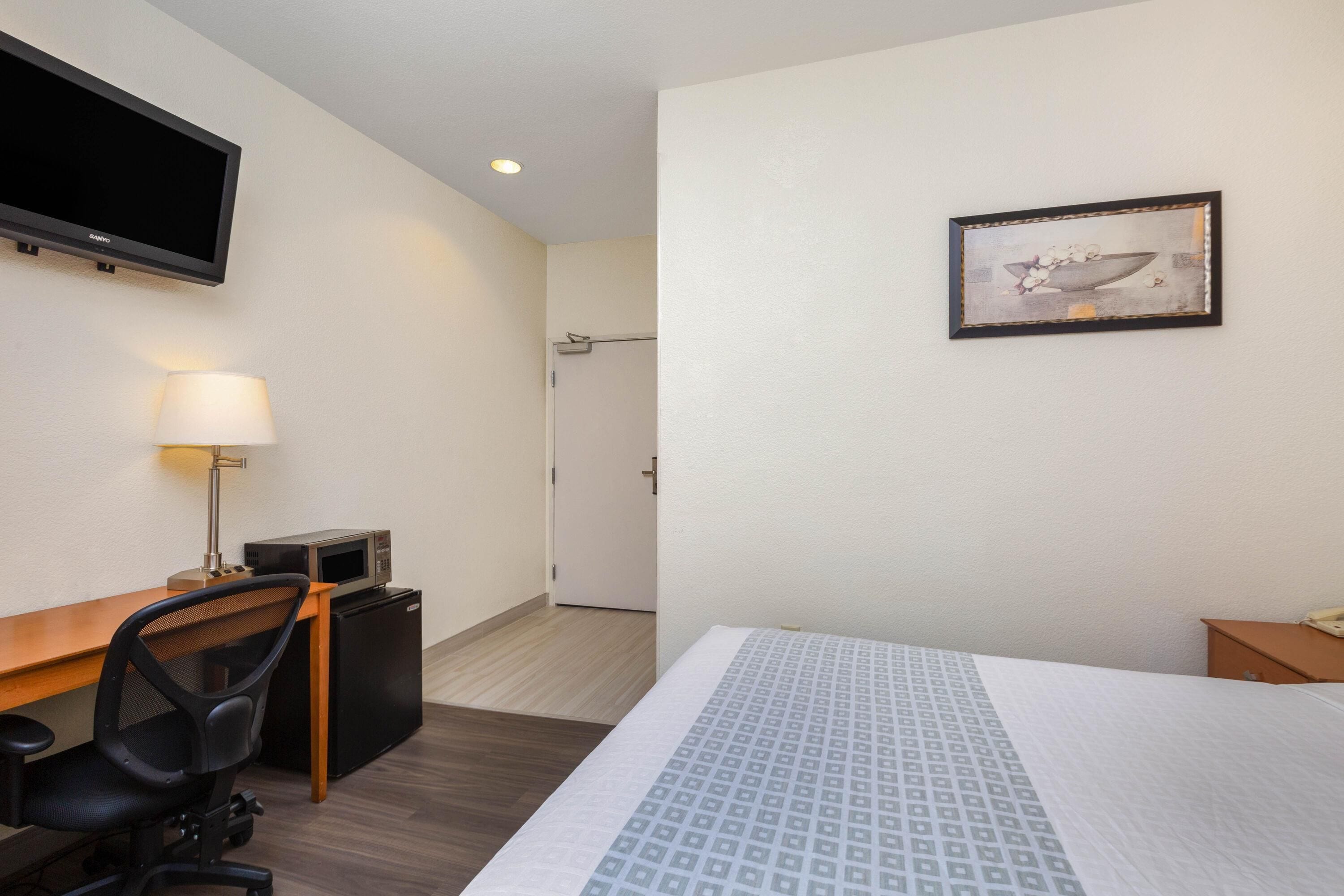 Habitación de hotel con cama, escritorio, silla, televisor y puerta que da a un baño.