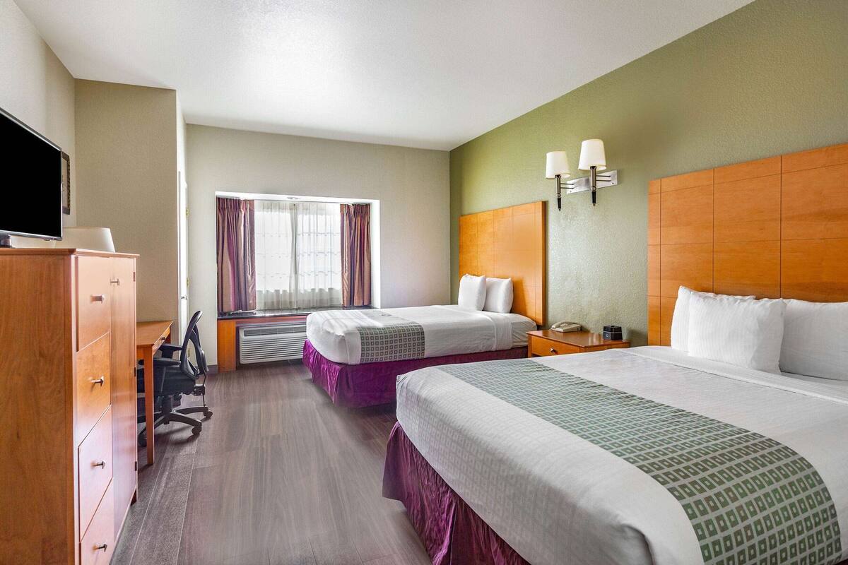 A hotel room with two beds, a desk, a television, and a window with curtains.