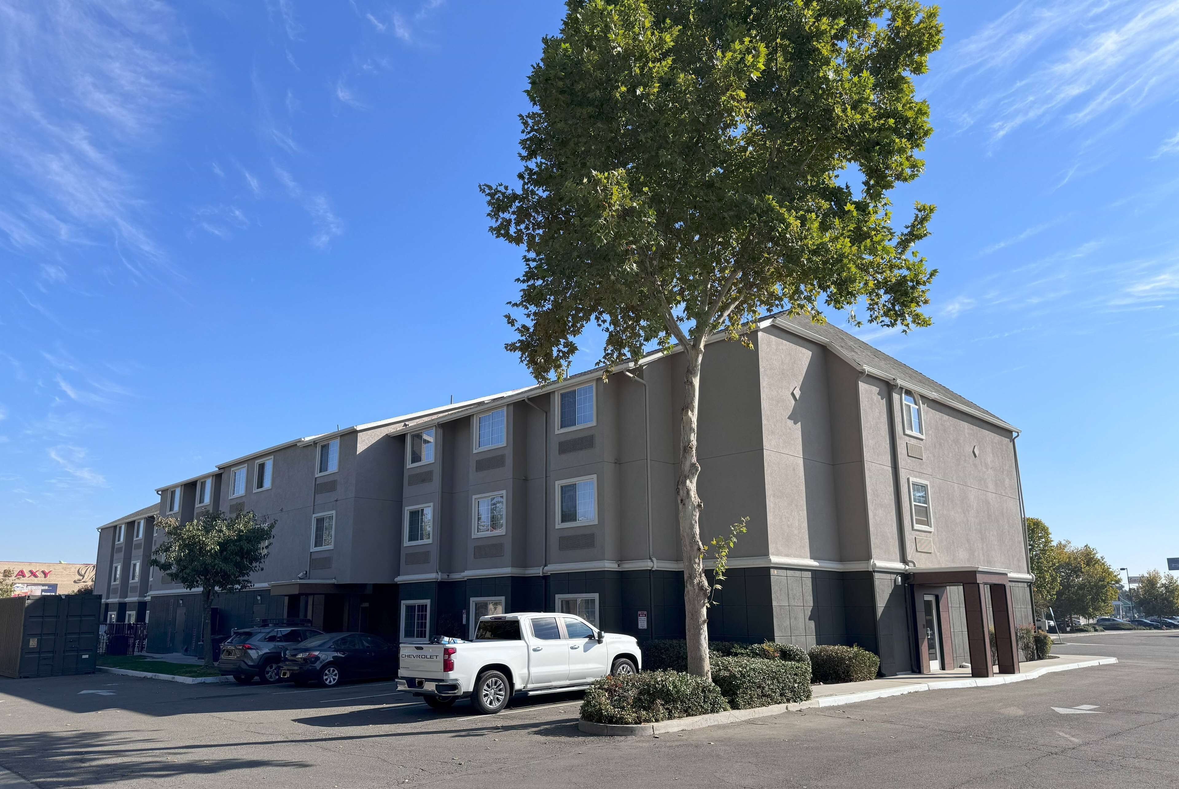 A multi-story building with a parking lot, a white pickup truck, and a tree in front.