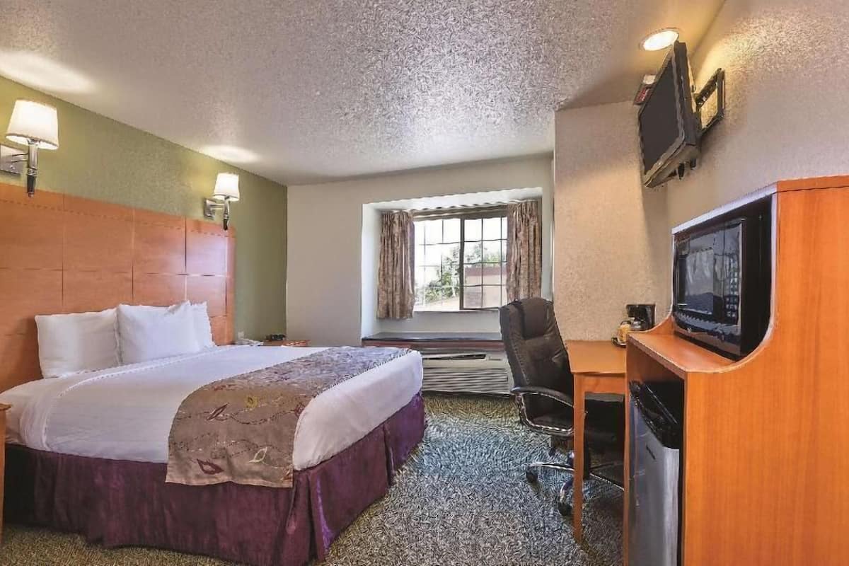 A hotel room with a bed, a desk with a television, a chair, and a window with curtains.