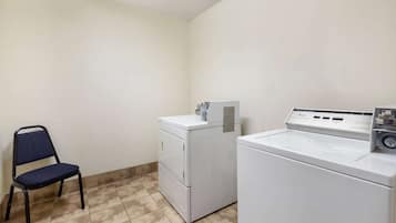 Un cuarto de lavandería con una silla, una lavadora de carga frontal y una lavadora y secadora apiladas.