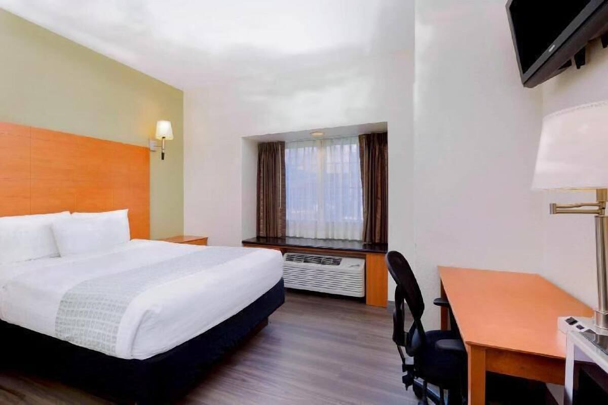 A hotel room with a bed, a desk, a chair, a TV, and a window with curtains.