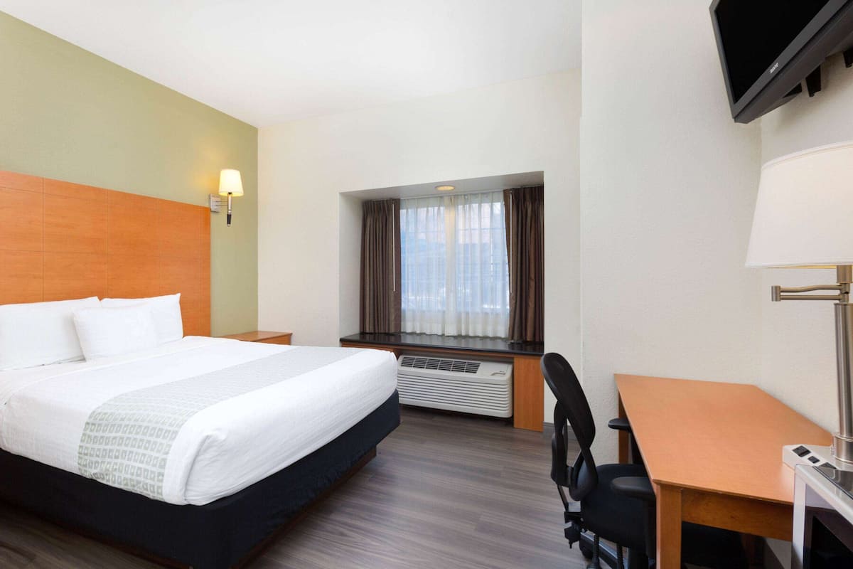 A hotel room with a bed, desk, chair, TV, and window with curtains.