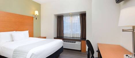 A hotel room with a bed, desk, chair, TV, and window with curtains.
