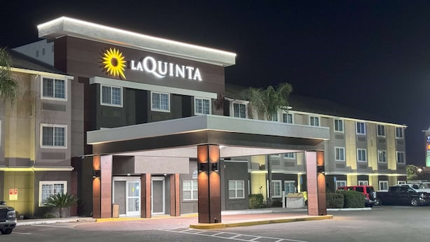 A La Quinta hotel with a modern design, featuring a prominent sun logo, a covered entrance, and a parking lot with several vehicles. - La Quinta Inn & Suites by Wyndham Tulare (Tulare)
