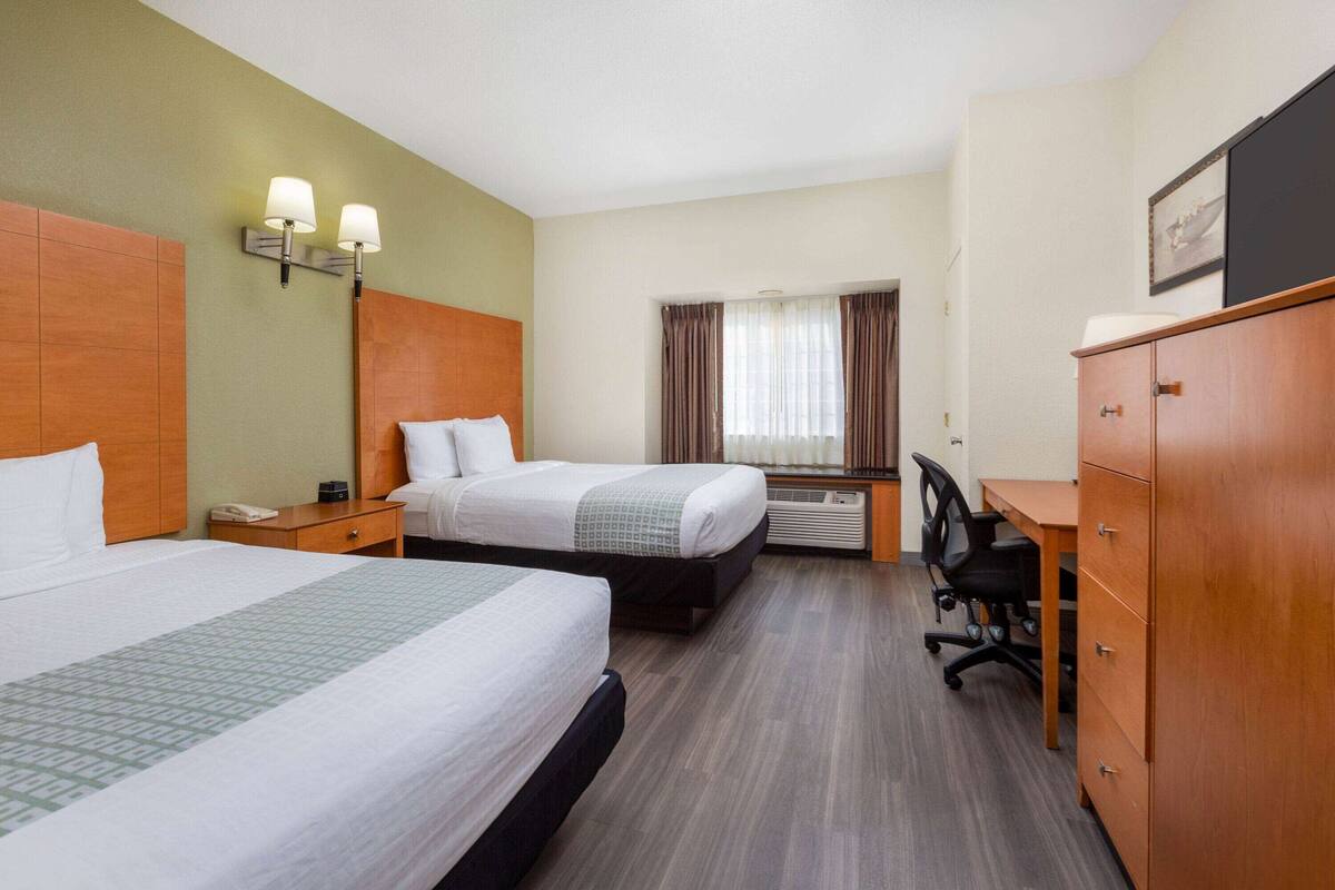 A hotel room with two beds, a desk, a chair, a wardrobe, and a window with curtains.