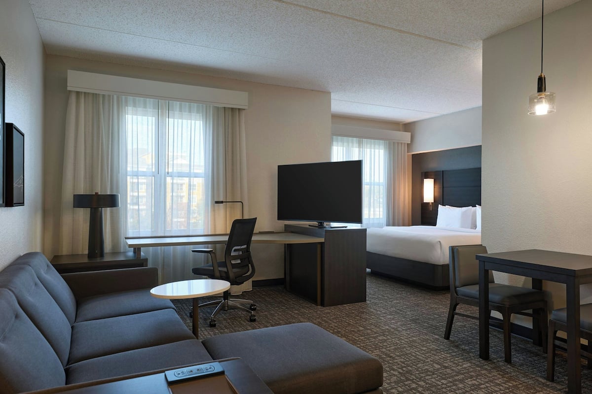 A hotel room with a sofa, a desk, a television, a bed, and a small table.