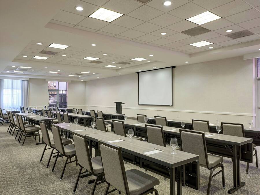 A conference room with long tables, chairs, and a projector screen.
