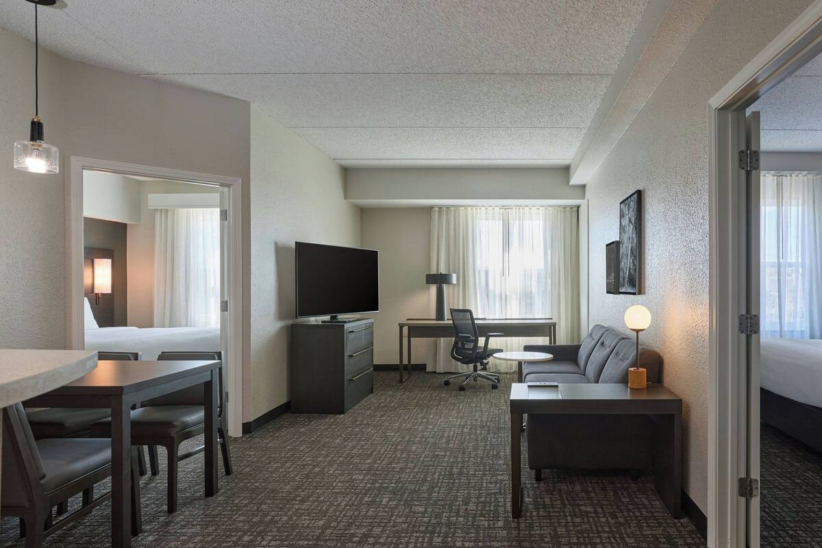 A hotel room with a bed, a desk, a TV, a sofa, and a dining table.