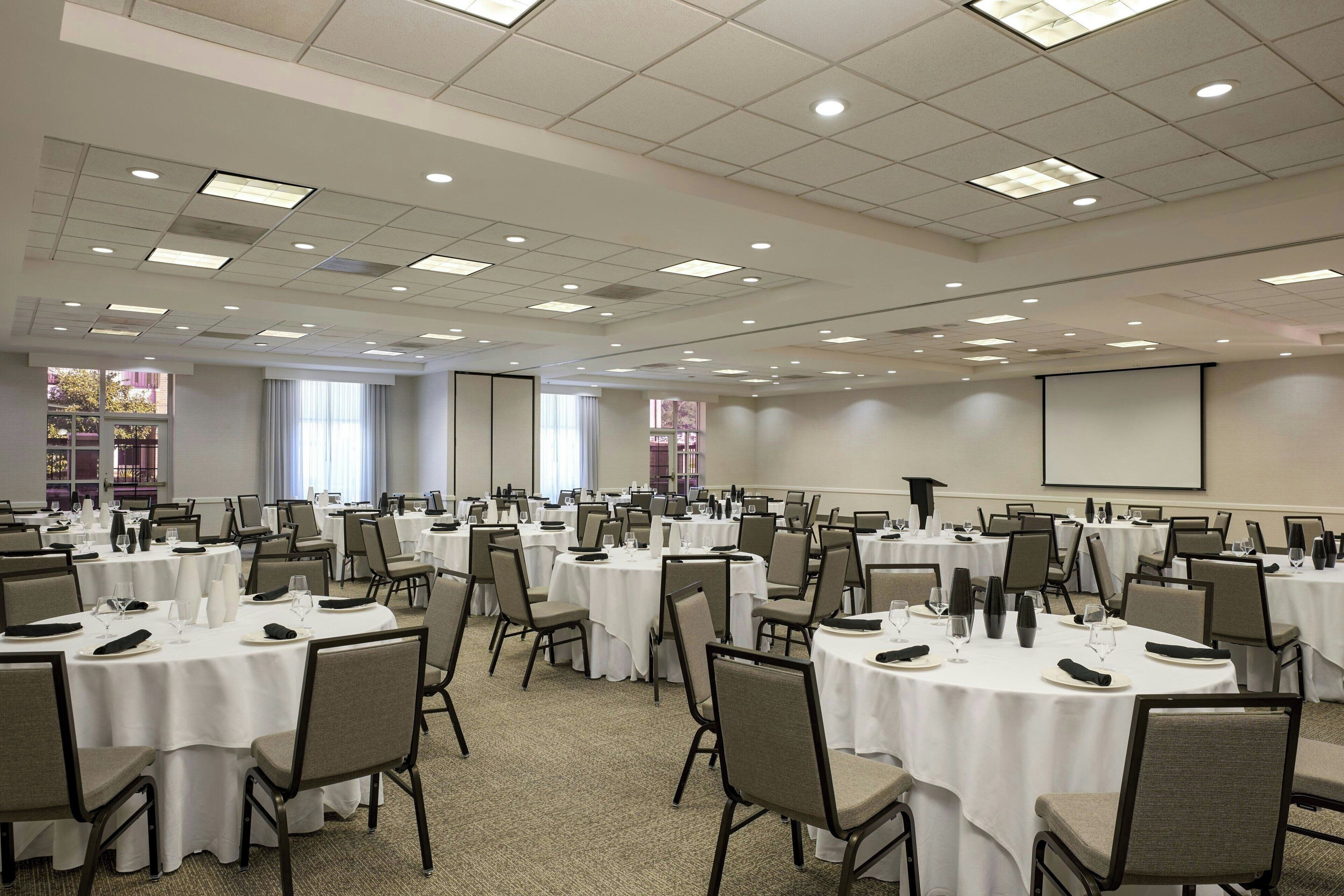 A large conference room with multiple round tables, each set with chairs, glasses, and plates.