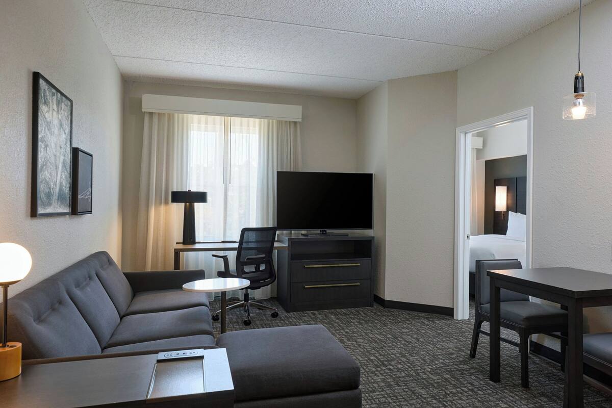 A hotel room with a sofa, a desk with a computer, a television, and a small table.