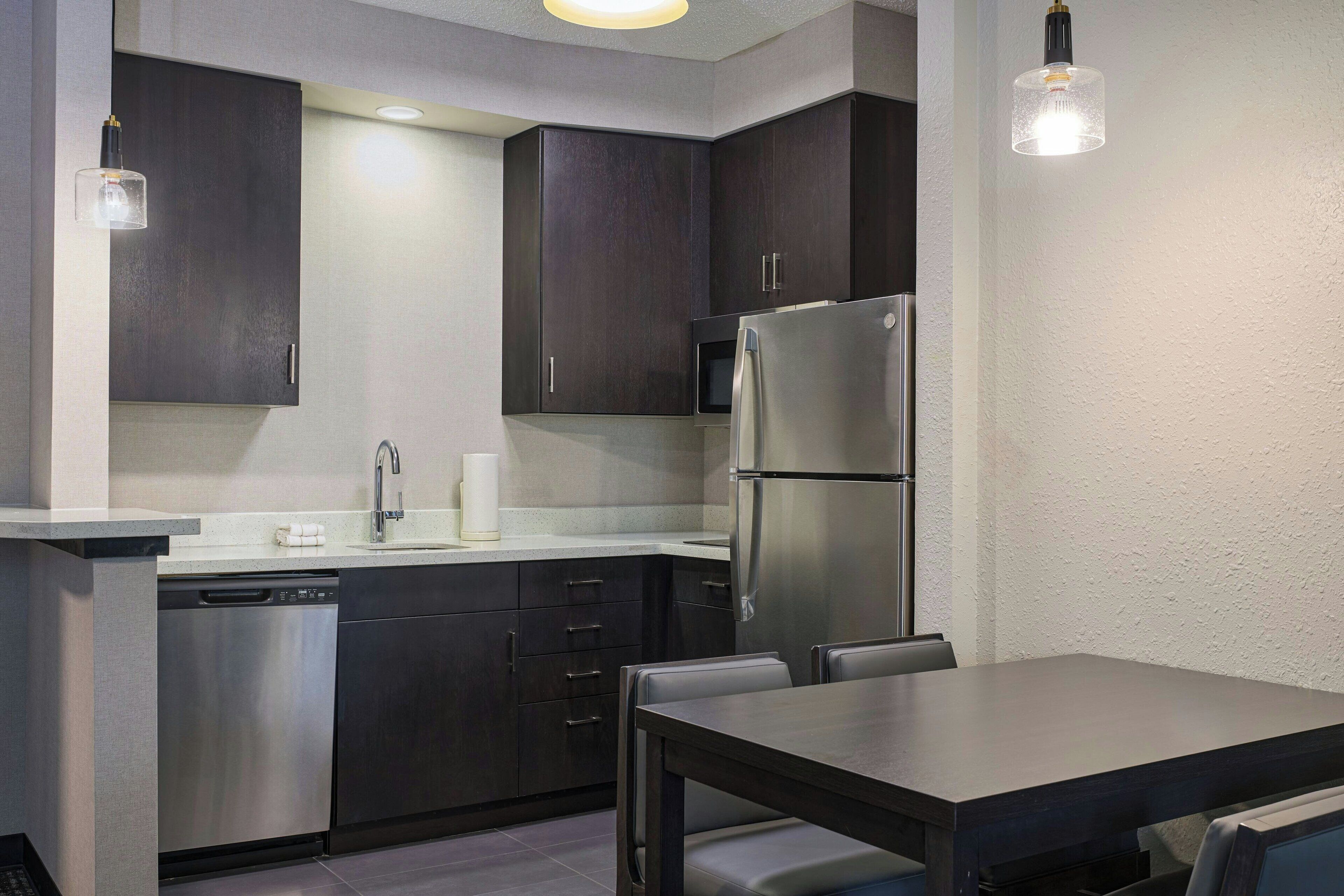 A modern kitchen with dark cabinets, stainless steel appliances, and a dining area with a table and chairs.