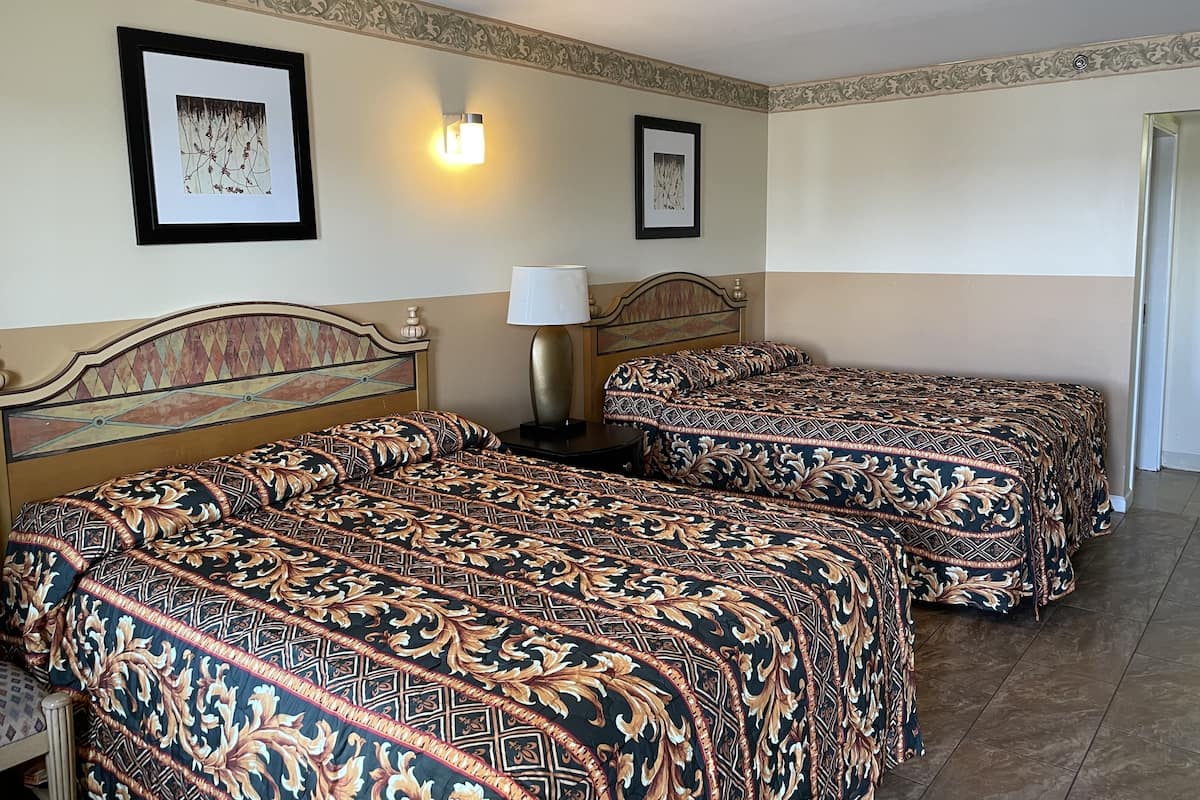 A hotel room with two beds, a nightstand with a lamp, and framed artwork on the walls.
