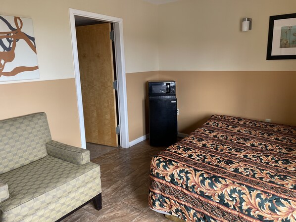 A room with a patterned bed, a sofa, a refrigerator, and a door leading to another room. - Sea Palace Inn (Seaside Heights)
