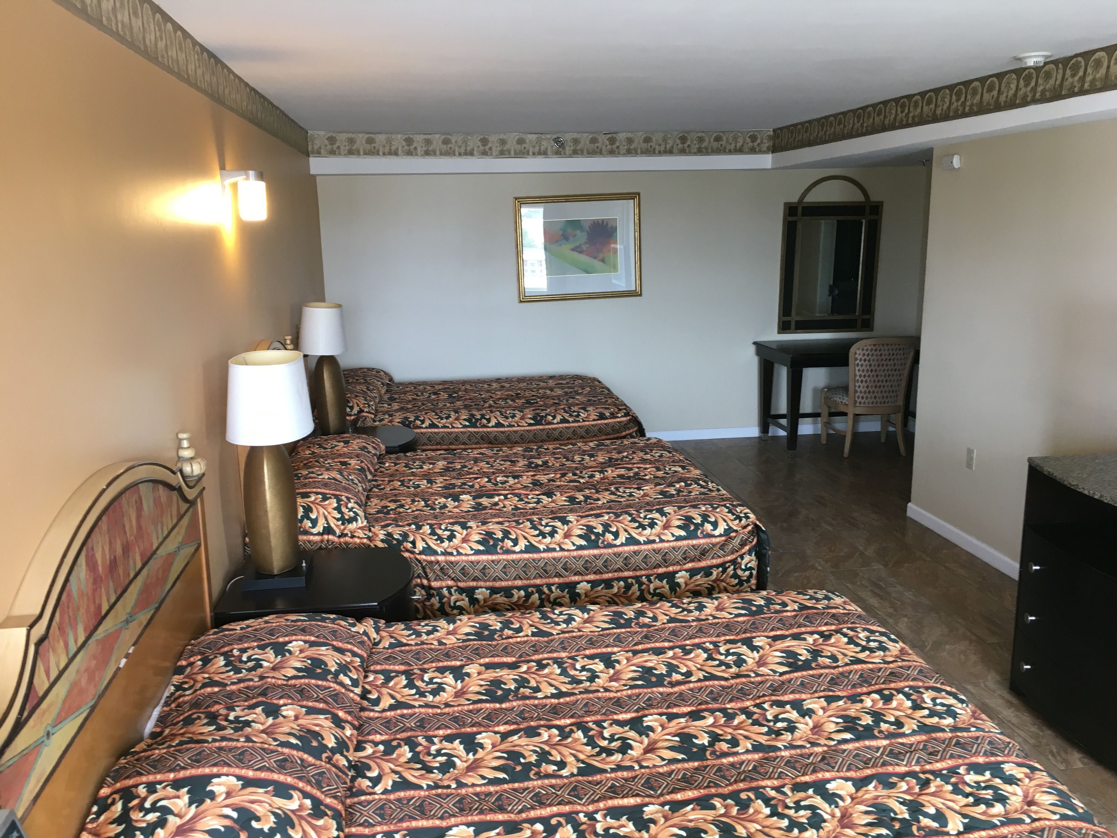 A hotel room with two beds, a desk, a chair, a lamp, and a painting on the wall.