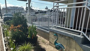 Un jardín con una escultura de pájaro, una cerca de metal y un edificio con toldo verde.