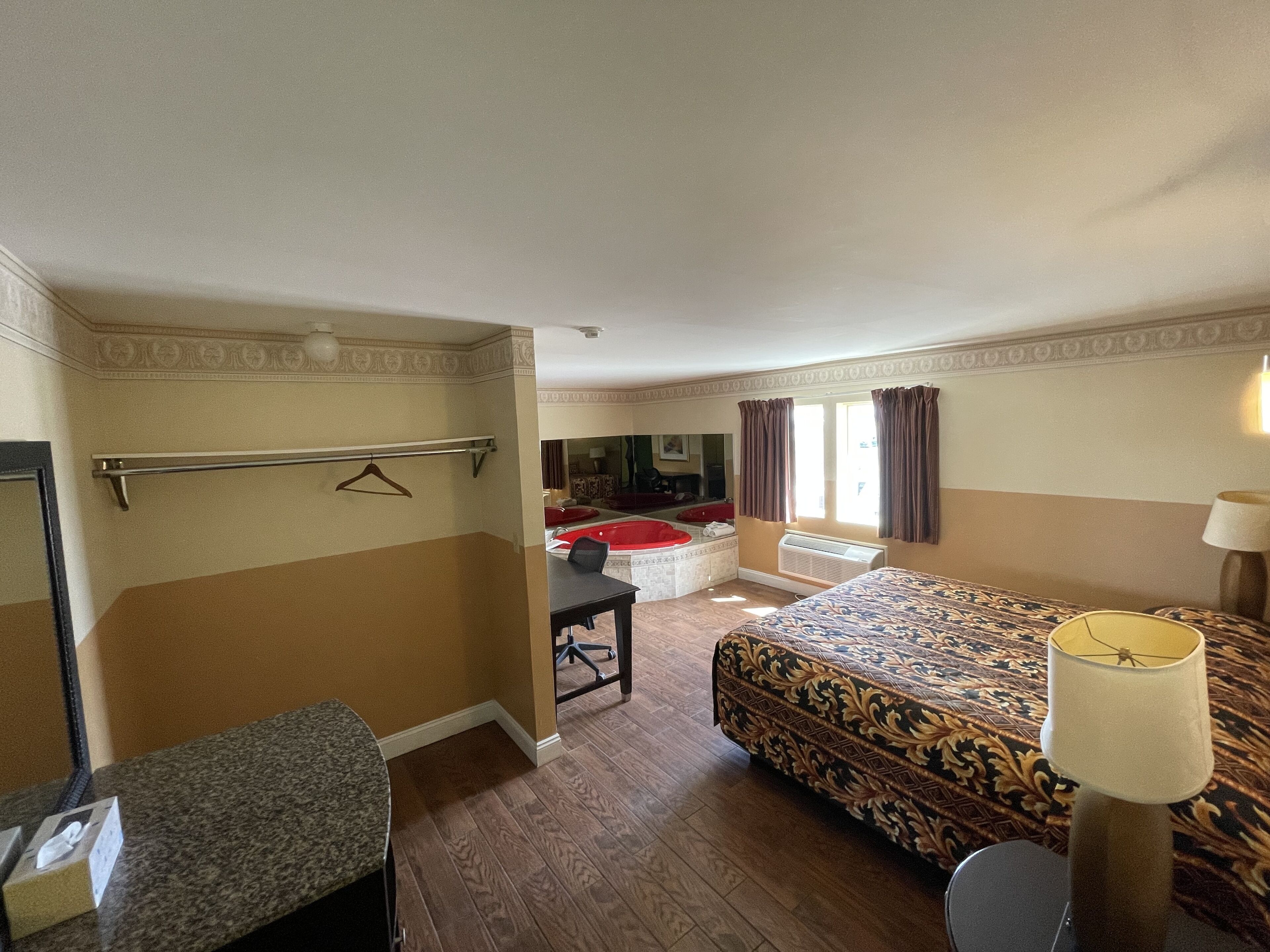 Habitación de hotel con cama, escritorio, silla, perchero y baño con bañera.