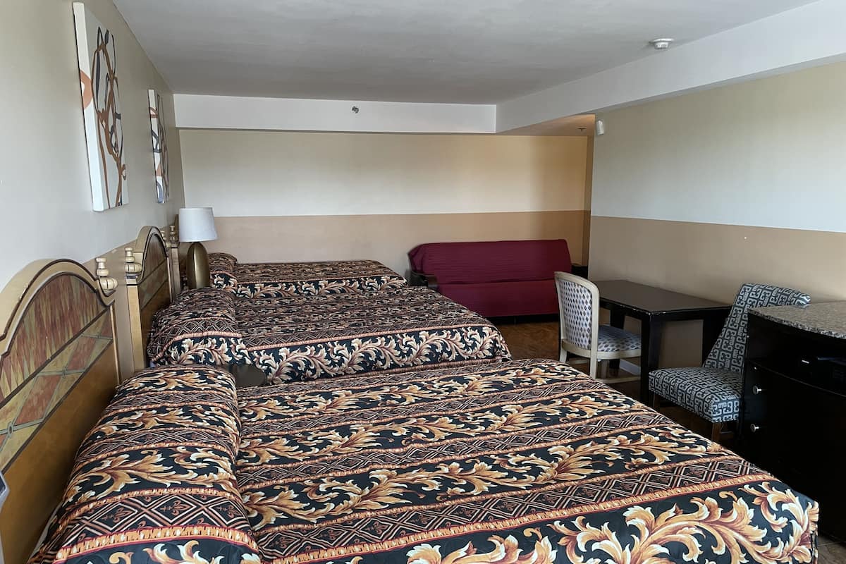 A hotel room with two beds, a red sofa, a desk, and a chair.