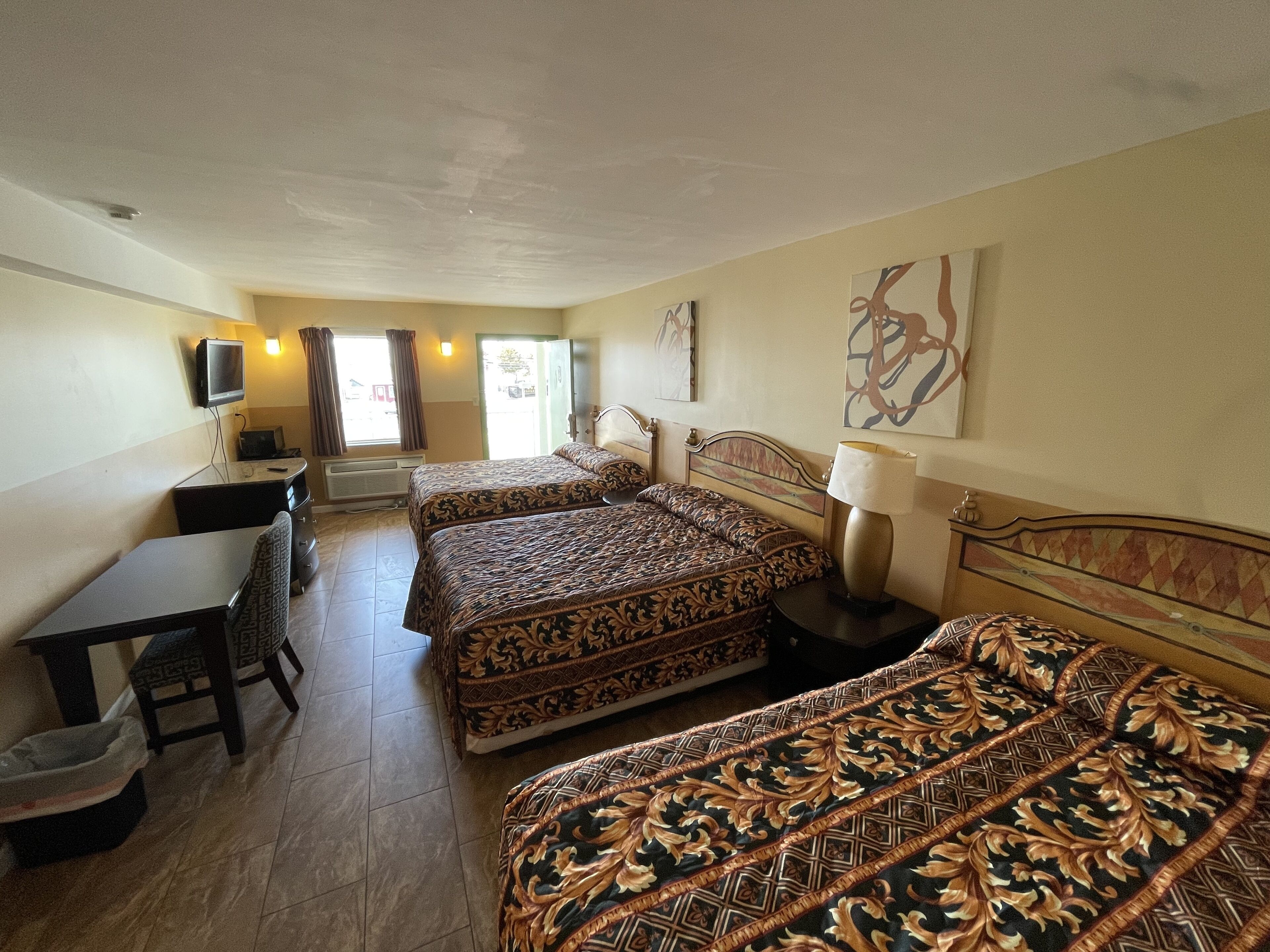 Habitación de hotel con dos camas, un escritorio, una silla, un televisor y una ventana con cortinas.