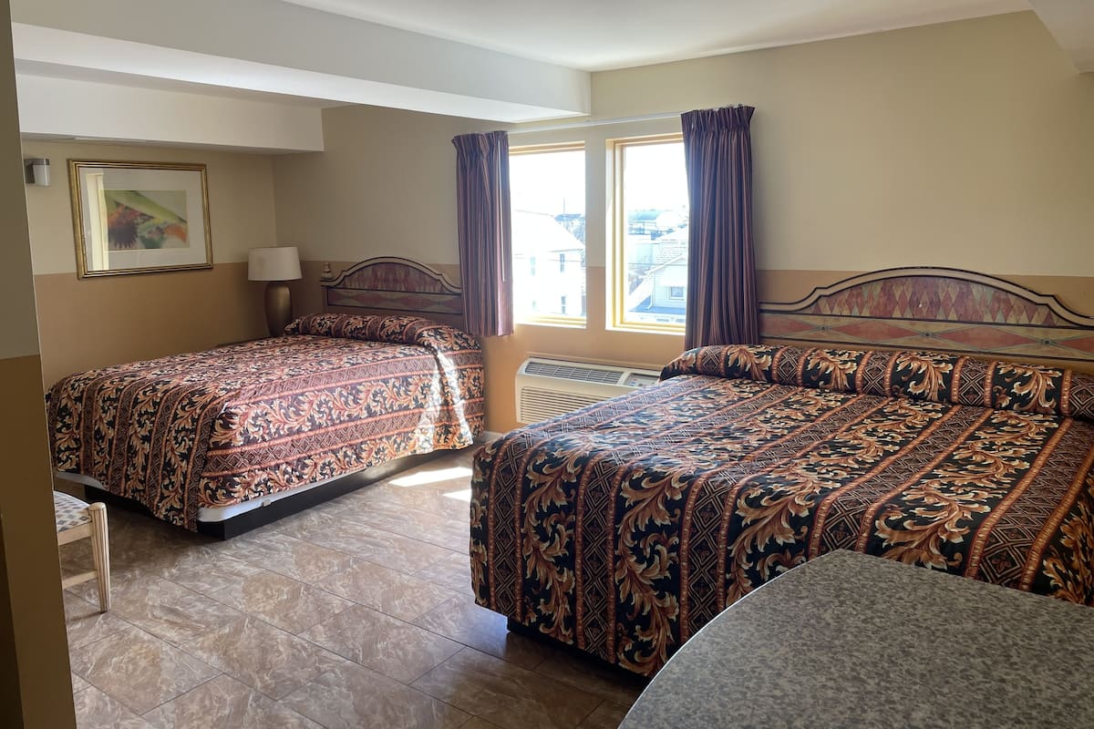 A hotel room with two beds, a window with curtains, a painting on the wall, and a ceiling light.