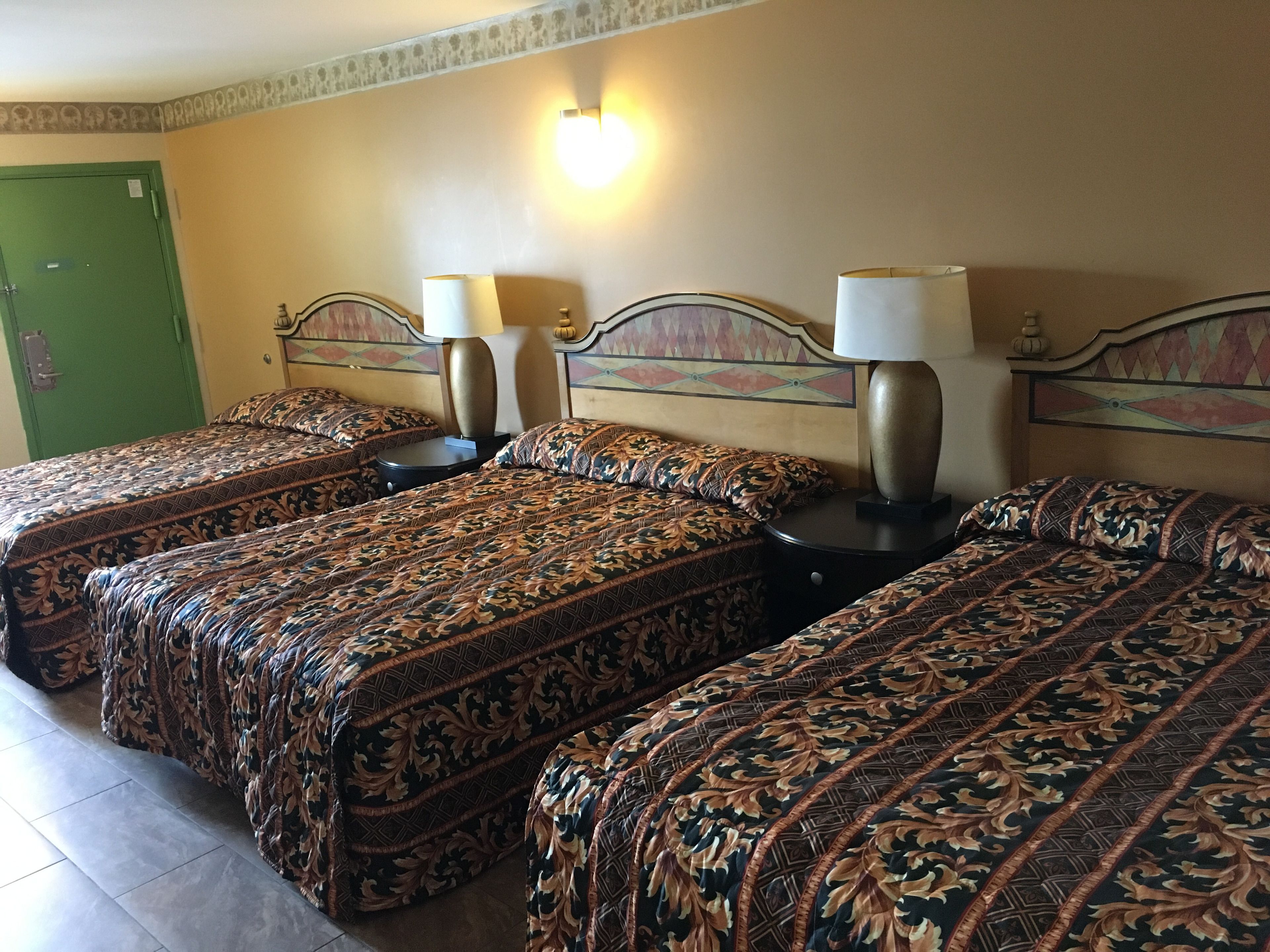 Een hotelkamer met drie bedden, elk voorzien van beddengoed met een patroon en nachtlampjes.