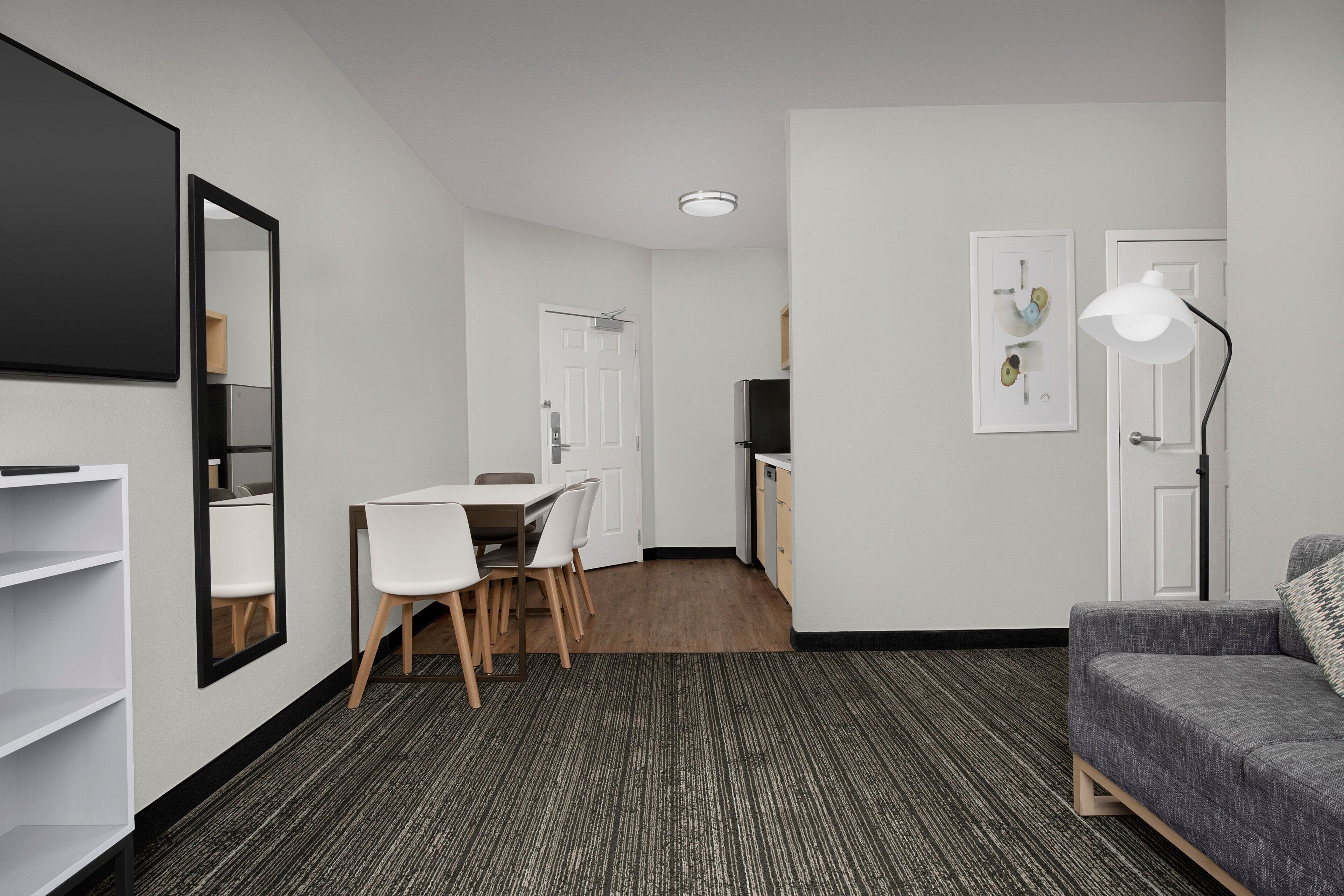 A modern hotel room with a dining area, a sofa, a large mirror, and a lamp.