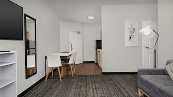 A modern hotel room with a dining area, a sofa, a large mirror, and a lamp.