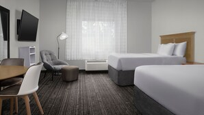 Ein Hotelzimmer mit Bett, Schreibtisch, Stuhl, Fernseher und einem Fenster mit Vorhängen.