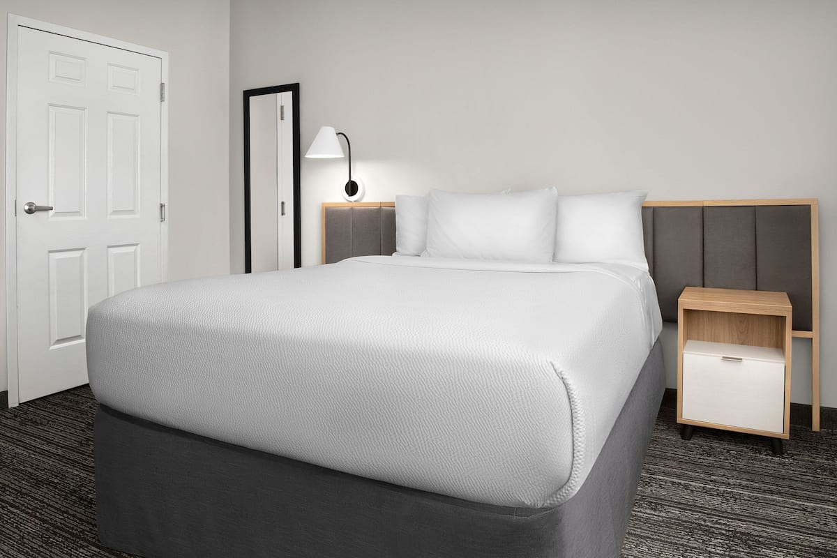 Una habitación de hotel con una cama grande, una mesita de noche y una lámpara.