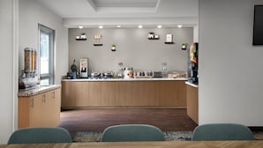 Eine moderne Küche mit Holzausbau, einer zentralen Kochinsel und verschiedenen Geräten. Im Vordergrund stehen zwei Stühle an einem Tisch.