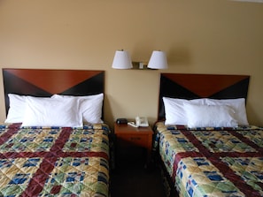 A hotel room with two beds, each with a quilted bedspread and white pillows. There are two bedside lamps and a telephone on the nightstand between the beds.