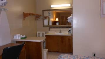 A hotel room with a bed, a desk, a chair, a sink, and a mirror.