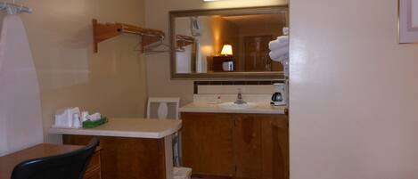 Una habitación de hotel con cama, escritorio, silla, lavabo y espejo.