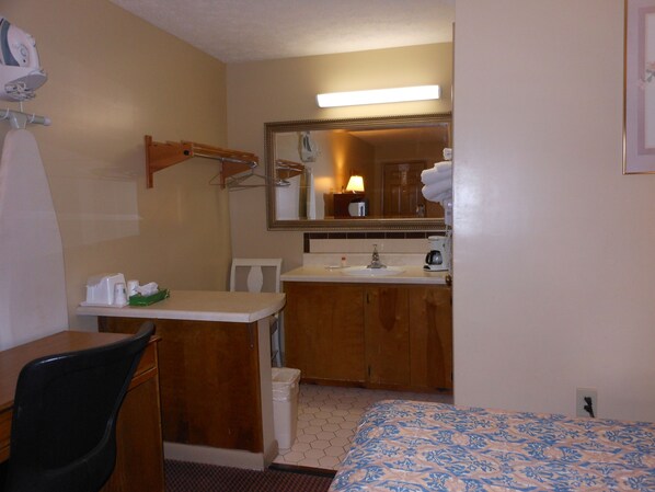A hotel room with a bed, a desk, a chair, a sink, and a mirror.