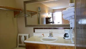 A bathroom with a sink, mirror, towel rack, chair, and a coffee maker. - McClellan Inn Anniston (Anniston)