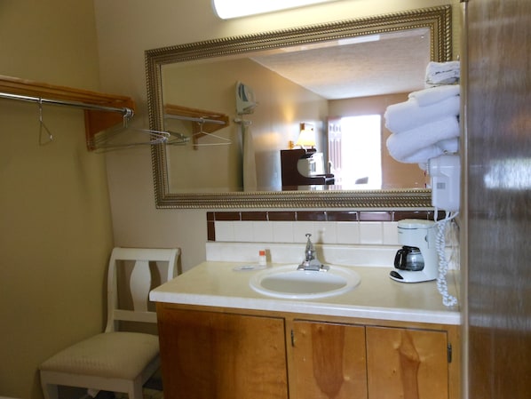 A bathroom with a sink, mirror, towel rack, chair, and a coffee maker. - McClellan Inn Anniston (Anniston)