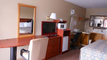 Een hotelkamer met een bed, bureau, stoel, magnetron en spiegel.