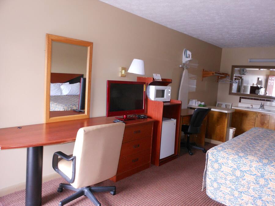 Een hotelkamer met een bed, bureau, stoel, magnetron en spiegel.