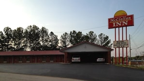 A McClellan Inn with a red and white sign, a parking lot, and a building with a red roof. - McClellan Inn Anniston (Anniston)