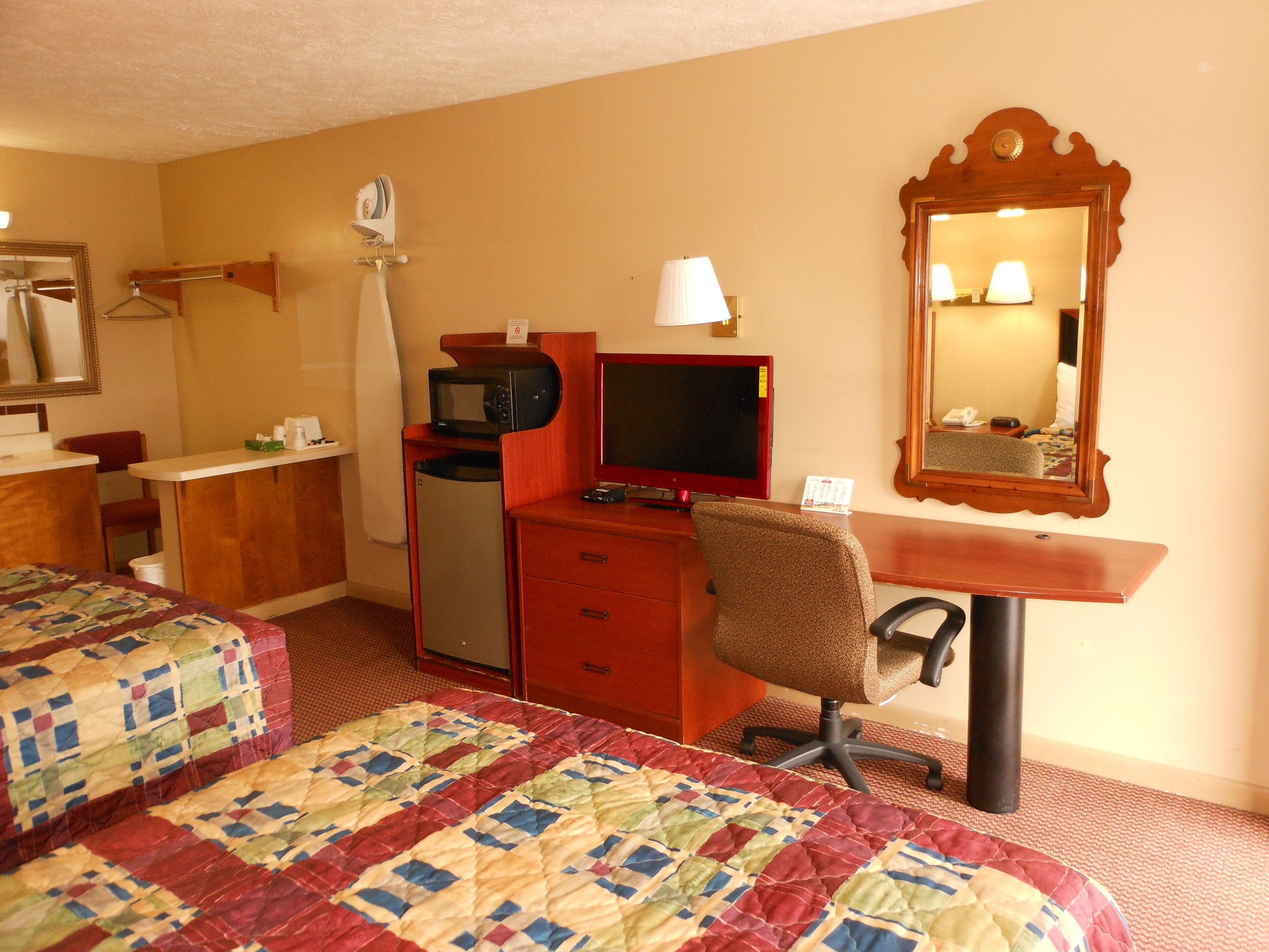 Una habitación de hotel con dos camas, un escritorio con una computadora, un televisor y un espejo.