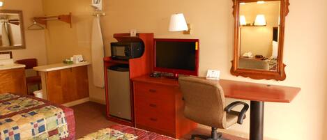 Una habitación de hotel con dos camas, un escritorio con una computadora, un televisor y un espejo.