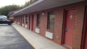 A motel with a row of rooms, each with a red door and a window. There is a parking lot with a few cars. - McClellan Inn Anniston (Anniston)