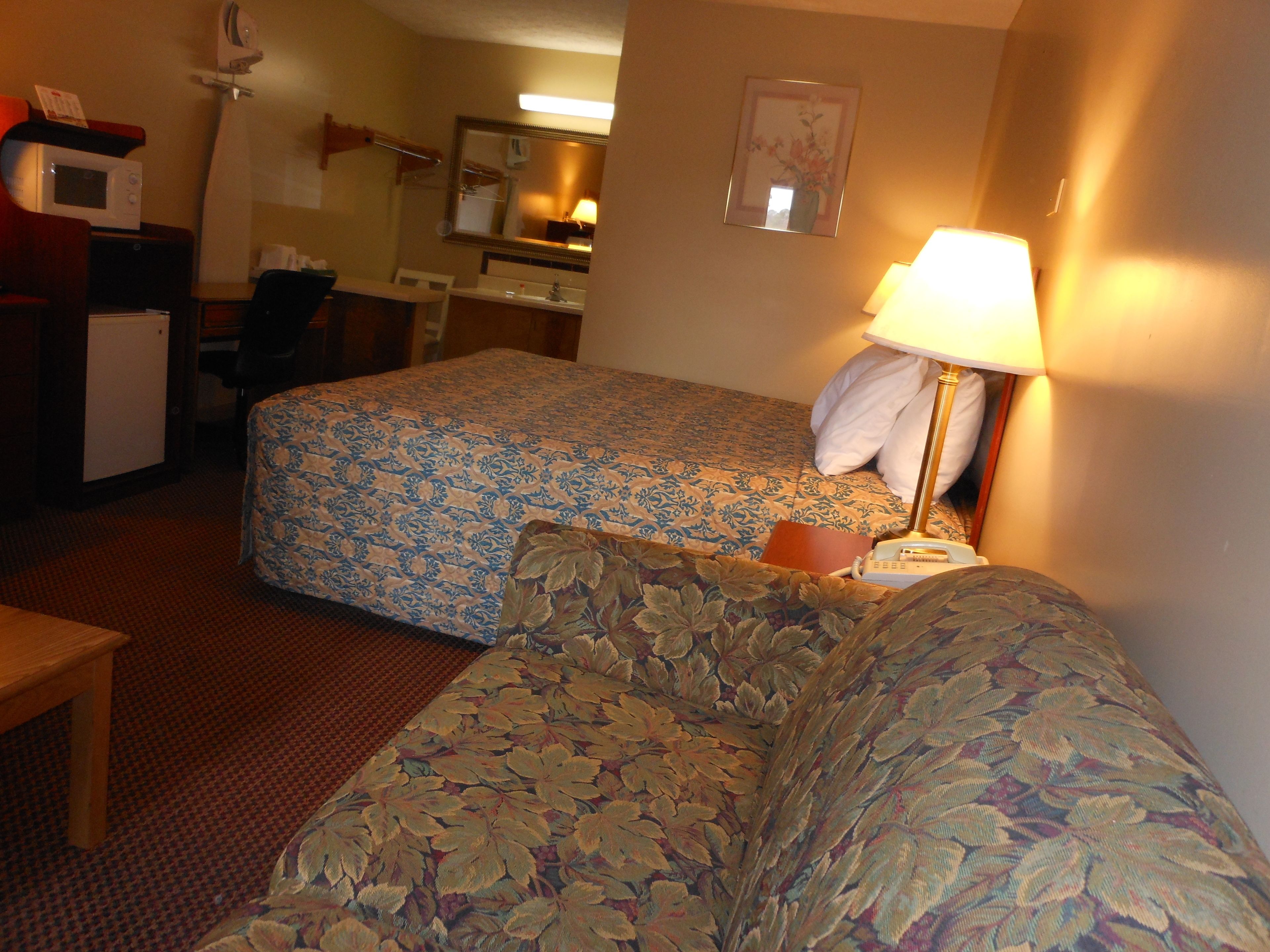 Une chambre d’hôtel avec deux lits, un bureau, une chaise, une lampe et un petit réfrigérateur.