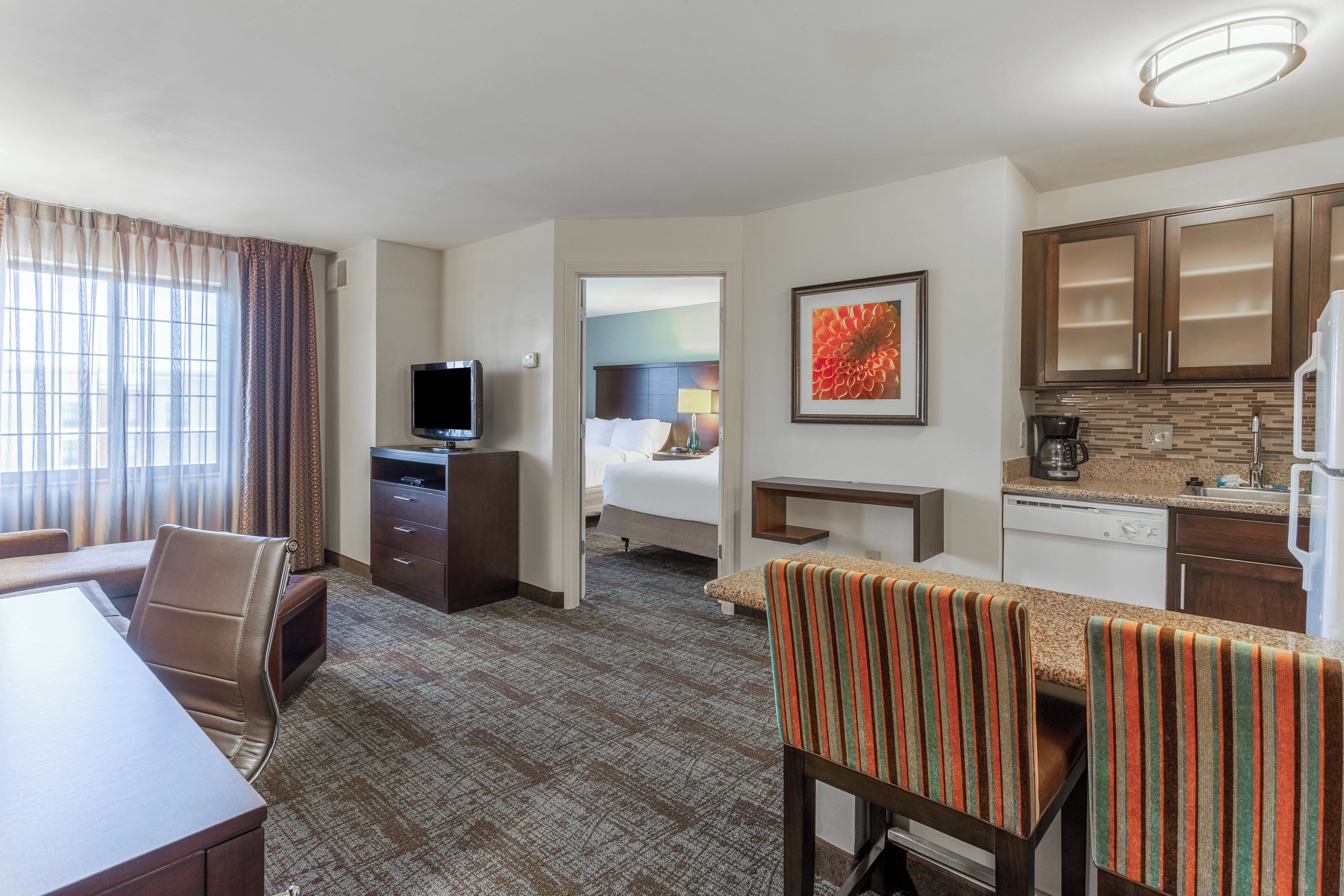 A hotel room with a dining area, a television, a bed, and a kitchen area.