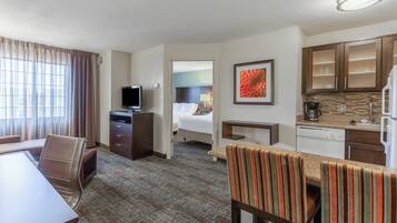 A hotel room with a dining area, a television, a bed, and a kitchen area.