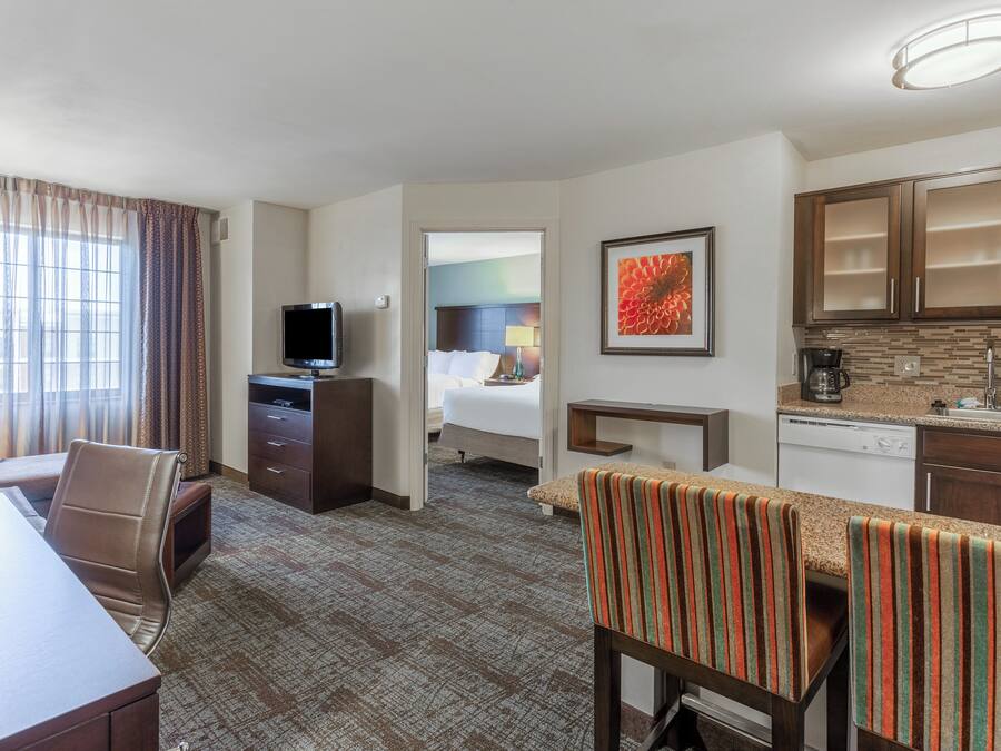 A hotel room with a dining area, a television, a bed, and a kitchen area.