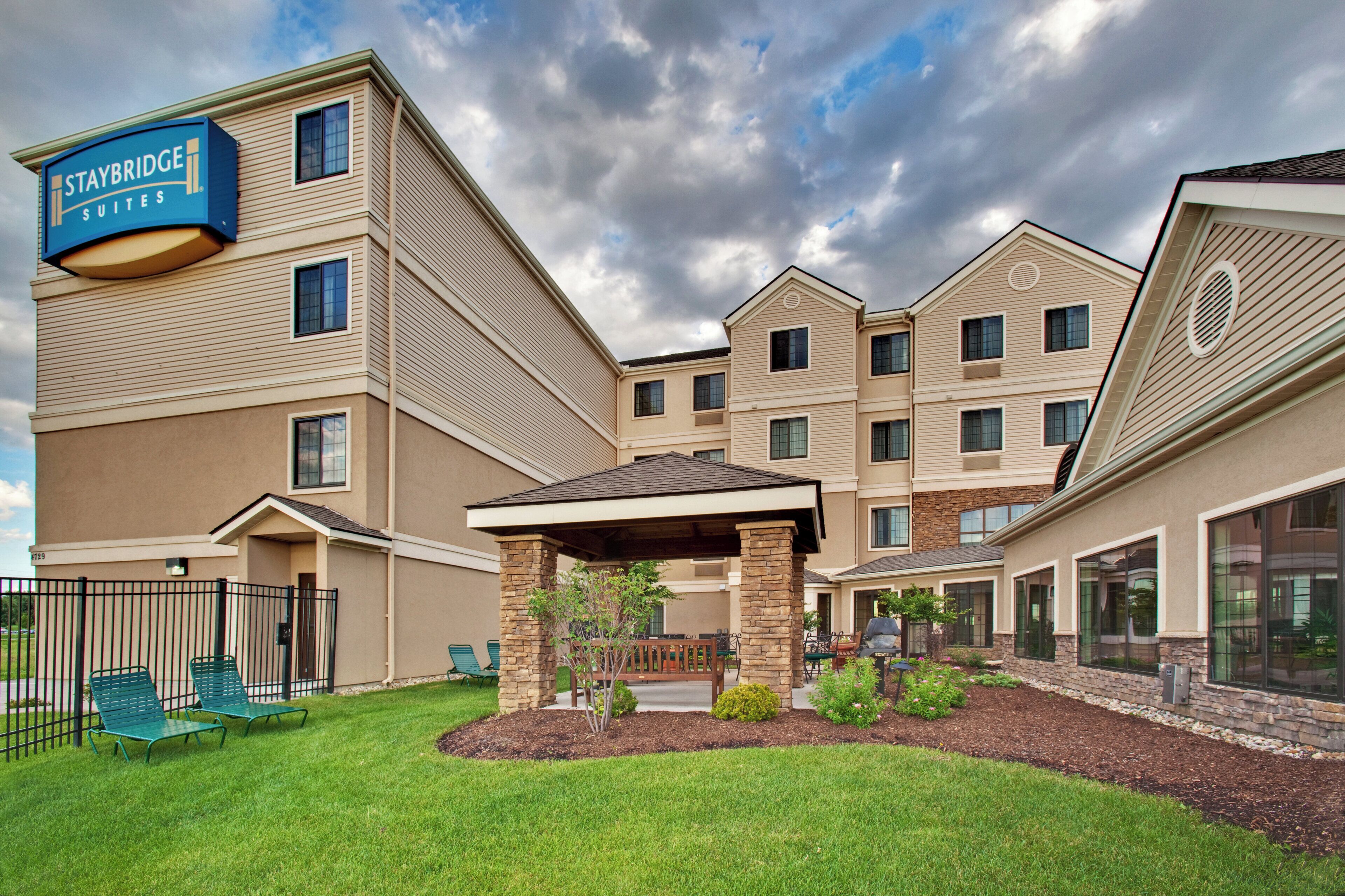 Un hotel Staybridge Suites con un patio cubierto, mobiliario exterior y un césped bien cuidado.