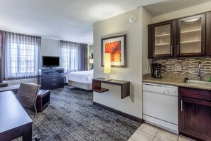 A hotel room with a bed, a desk, a television, a coffee maker, and a kitchen area with cabinets and a sink. - Staybridge Suites Davenport by IHG (Davenport)