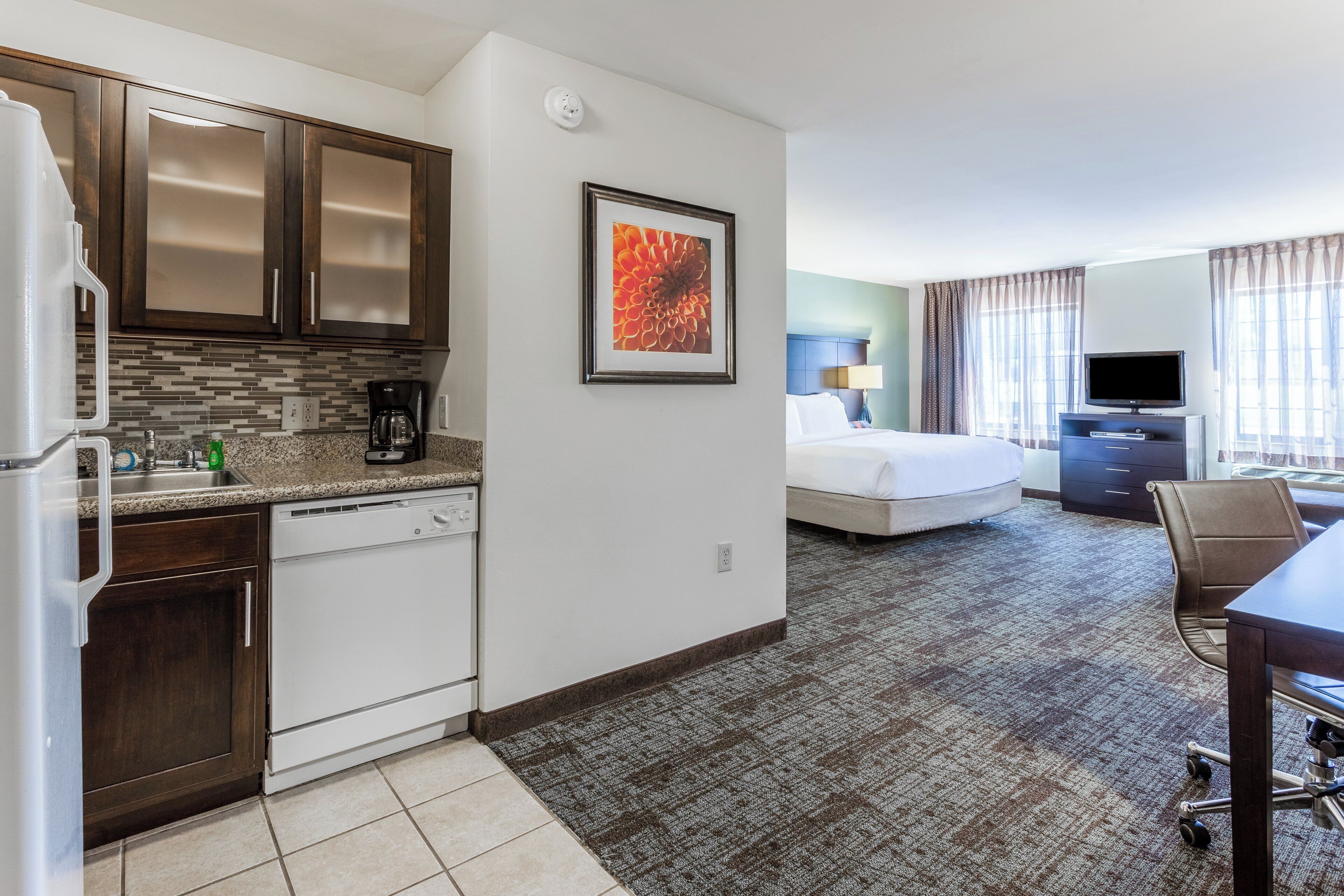 A hotel room with a kitchenette, a bed, a desk, and a television.
