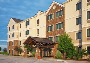 A multi-story hotel with a central entrance featuring a covered walkway and a stone pillar.